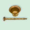 Mortero de bronce antiguo con la maja colocada al lado, destacando su diseño artesanal. Pieza decorativa auténtica y funcional.