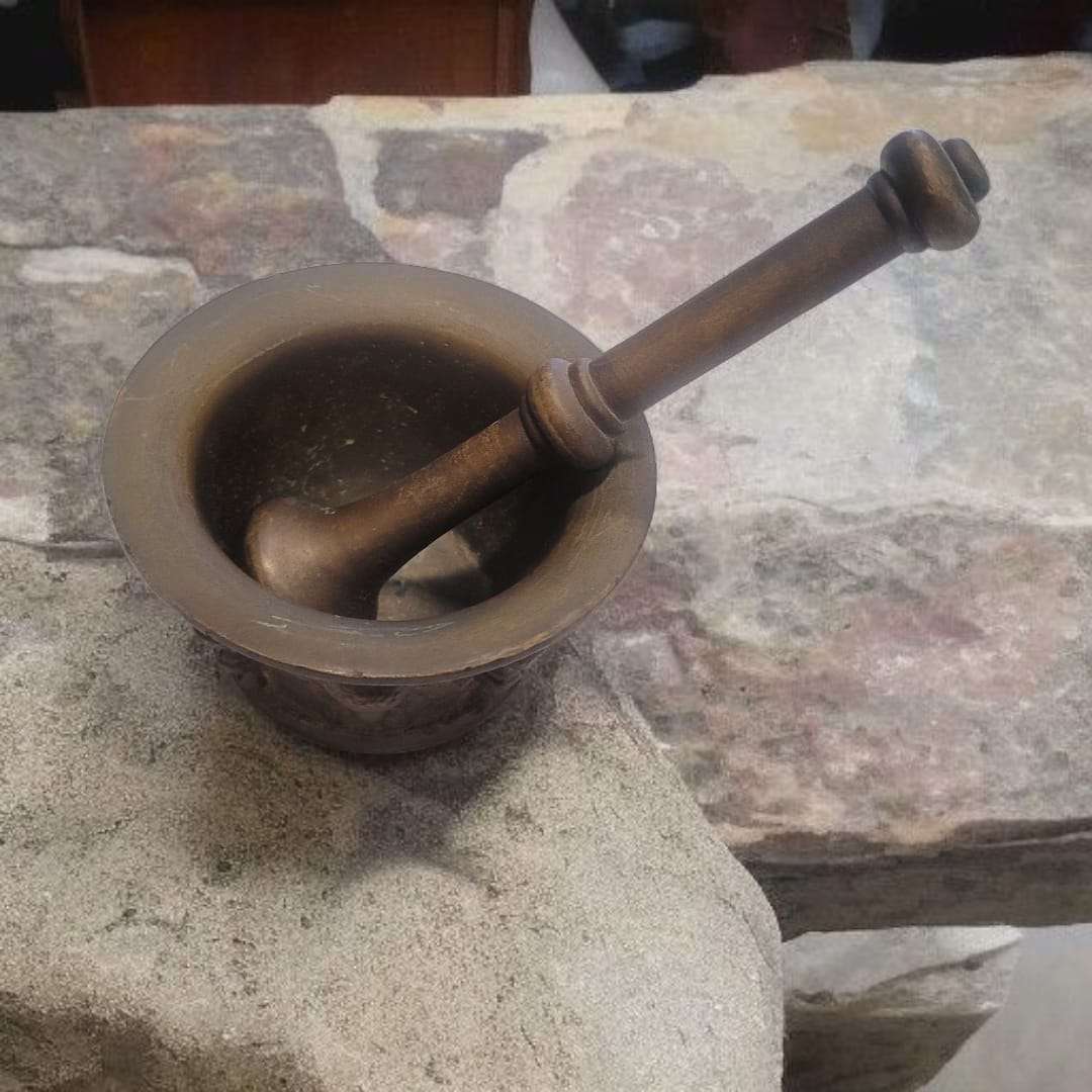 Mortero de bronce antiguo con maja artesanal sobre piedra rústica. Ideal para cocina tradicional o decoración vintage de hogar.