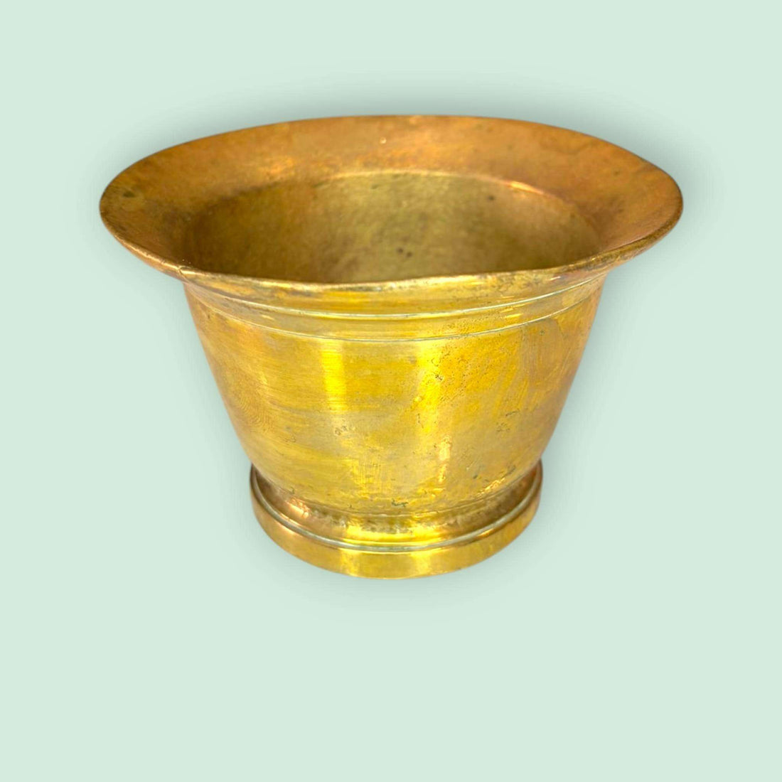 Mortero de bronce antiguo con maja original única sobre fondo verde claro. Ideal para decoración rústica o cocina tradicional.