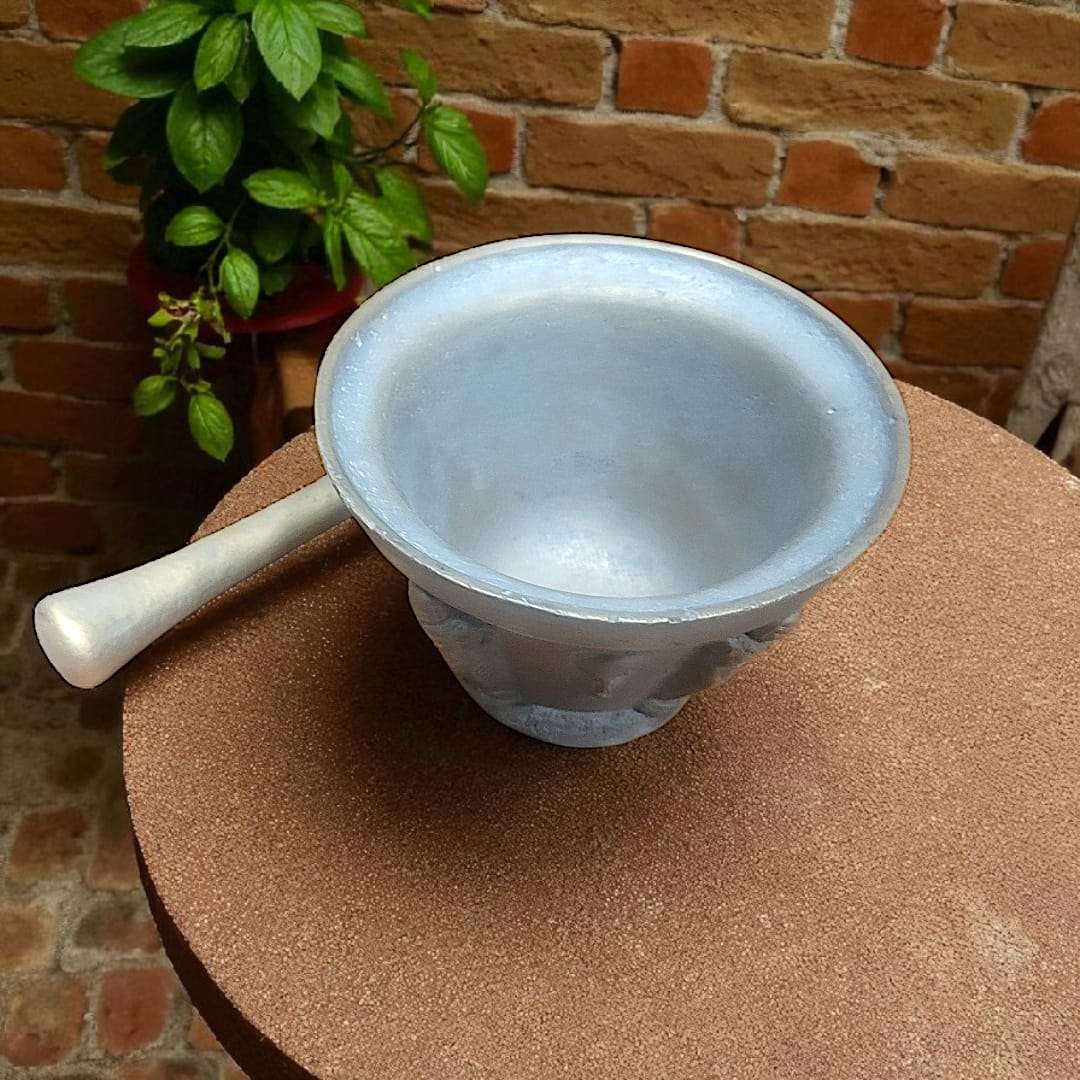 Mortero antiguo de bronce con relieves y maja única sobre mesa rústica. Decoración vintage ideal para cocina o jardín en estilo clásico.