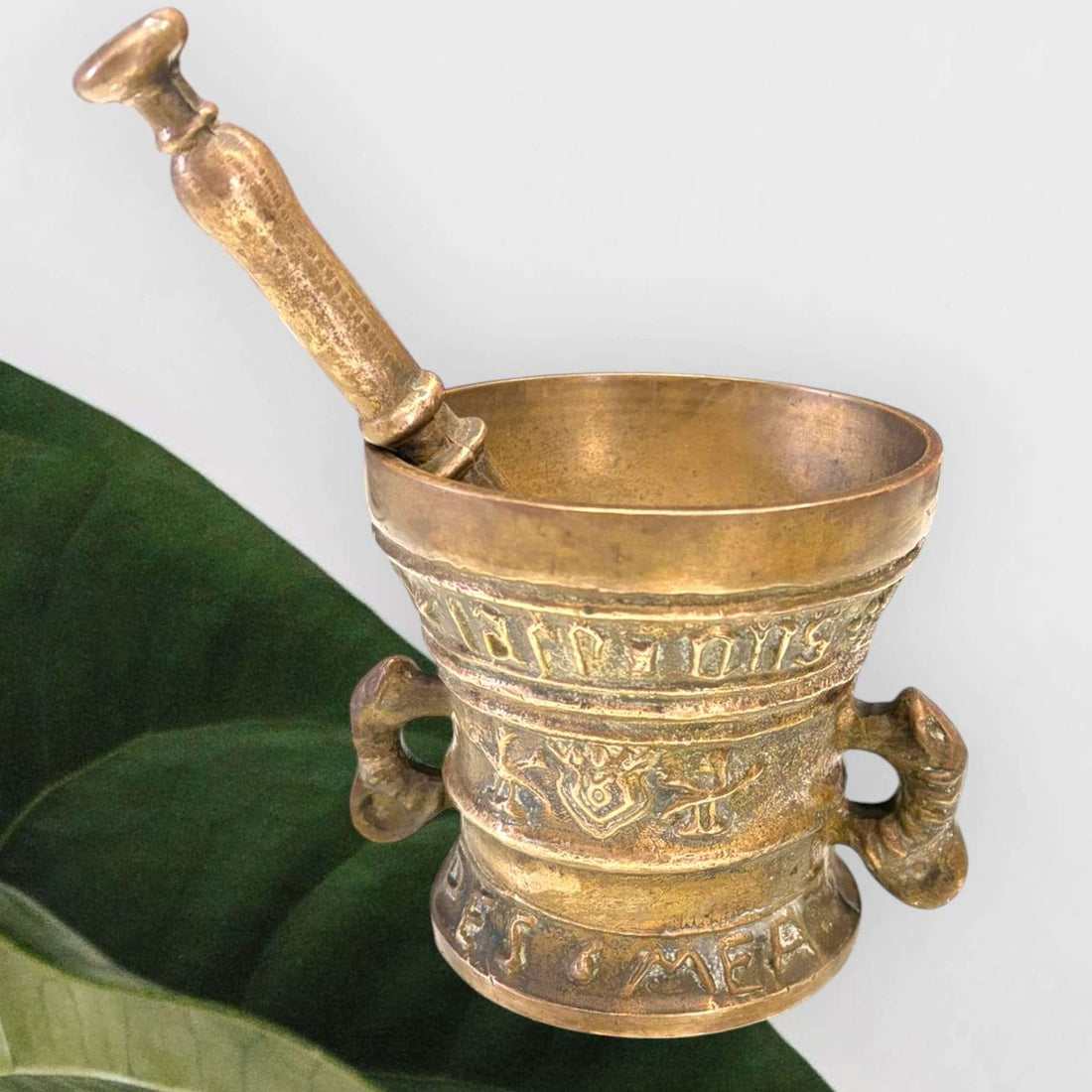 Mortero de bronce antiguo con relieves y maja original, ideal para decoración vintage en el hogar. Diseño artesanal con asas ornamentales.