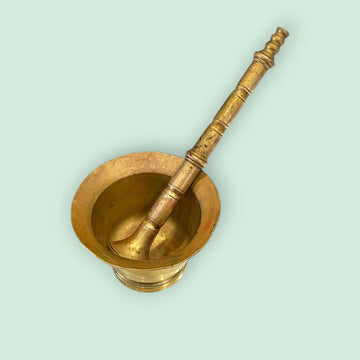 Mortero de bronce antiguo con maja original única sobre fondo verde claro. Ideal para decoración rústica o cocina tradicional.