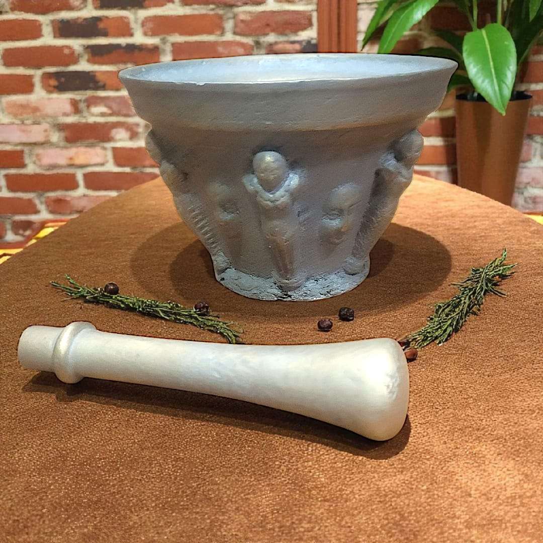 Mortero antiguo de bronce con relieves figurativos y maja única sobre mesa de terciopelo. Ideal para decoración vintage en hogar o jardín.