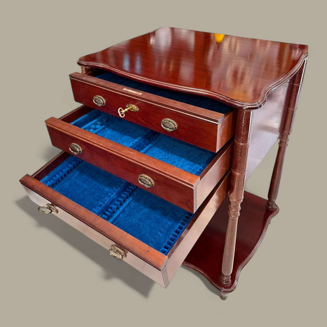 Mueble cubertero de madera con tres cajones, llave y acabado brillante, ideal para decoración elegante en el hogar. Diseño clásico con patas torneadas.