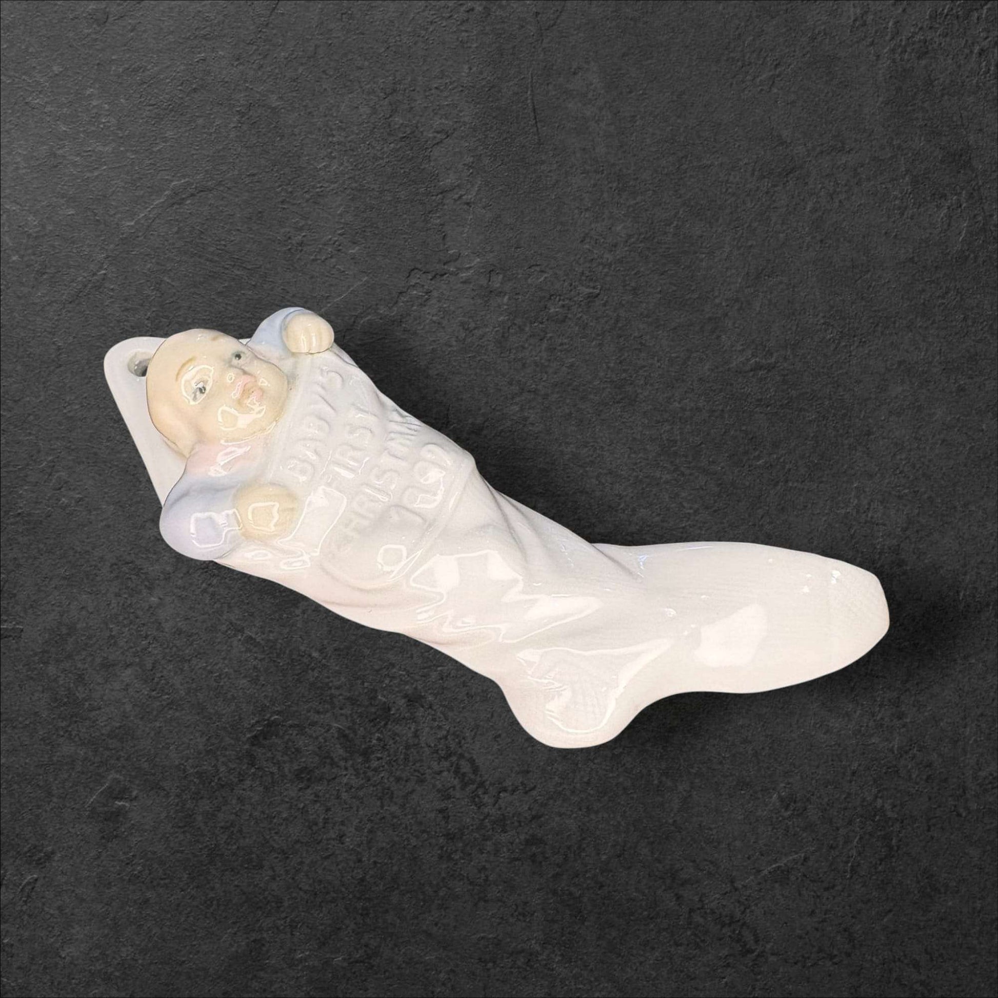 Figura decorativa Lladró de porcelana con bebé sonriente en calcetín navideño. Objeto de colección 'La primera Navidad del bebé'.