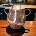 Olla de cobre antigua martilleada con tapa y asas, ideal para decoración rústica en cocinas o comedores vintage. Pieza artesanal brillante y única.