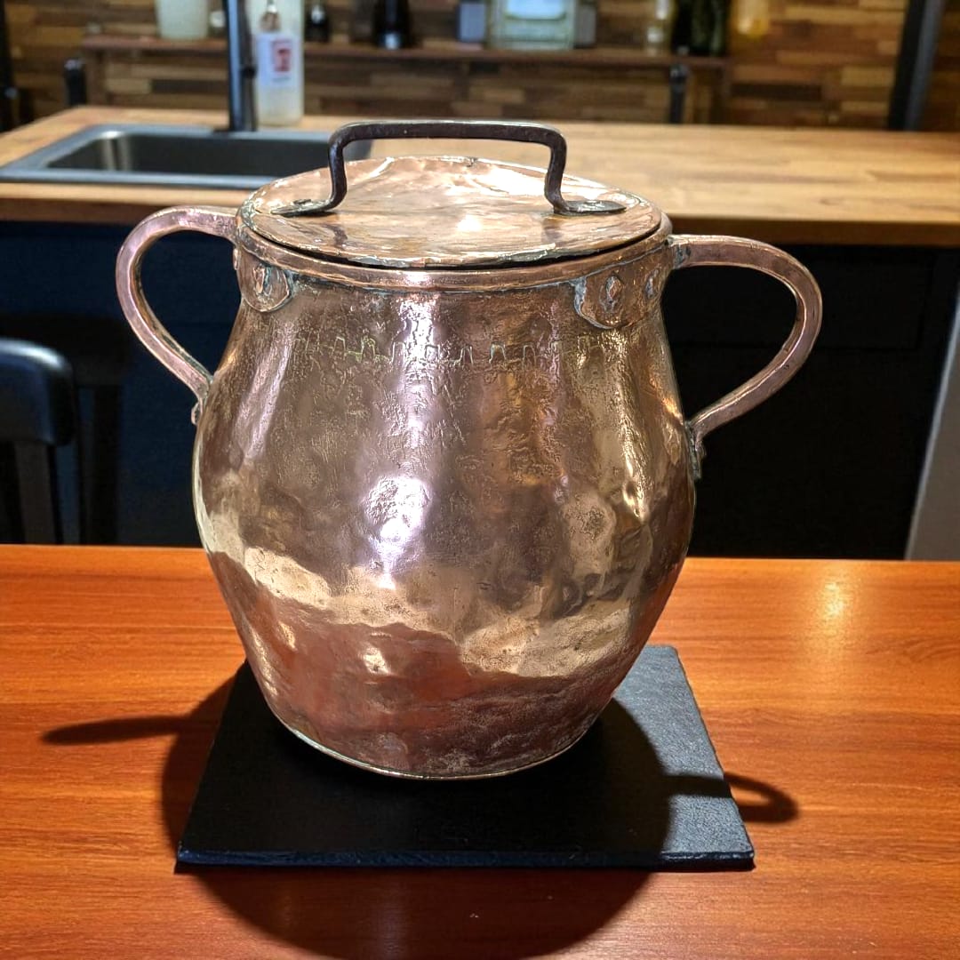 Olla de cobre antigua martilleada con tapa y asas, ideal para decoración rústica en cocinas o comedores vintage. Pieza artesanal brillante y única.