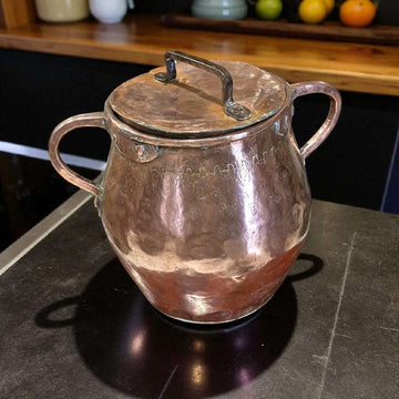 Olla de cobre antigua martilleada con tapa y asas, ideal para decoración rústica de cocina o colección vintage. Diseño artesanal y acabado brillante.