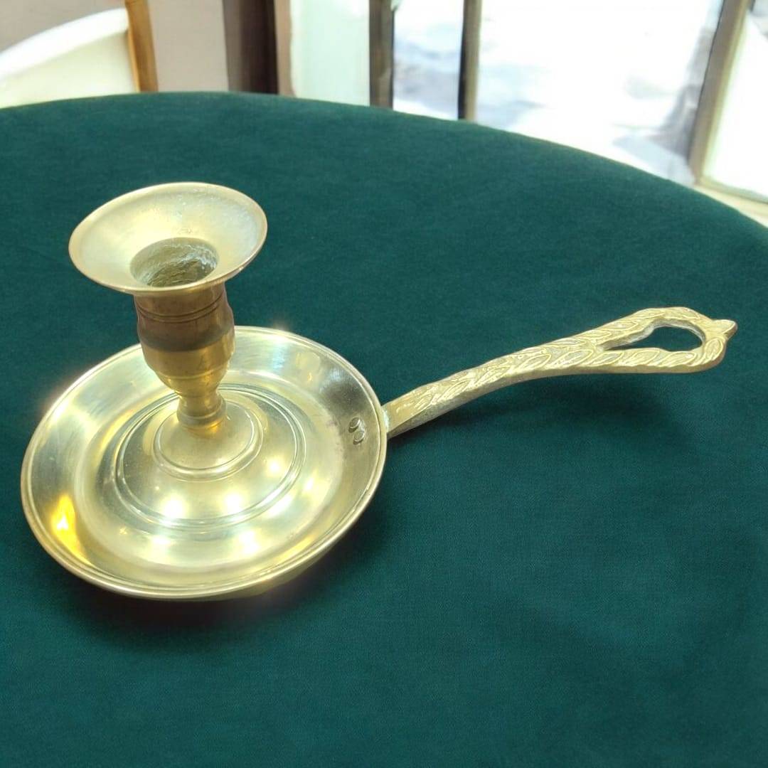 Palmatoria de metal dorado con mango calado grabado vintage sobre mantel verde. Diseño clásico ideal para decoración de interiores elegantes.