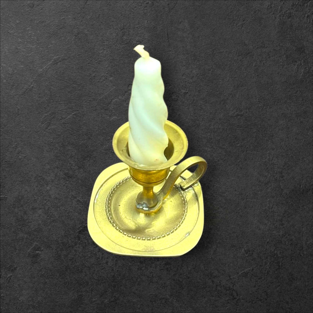 Palmatoria de metal dorado pequeña, vintage y decorativa con vela blanca en espiral sobre fondo oscuro. Ideal para decoración clásica del hogar.