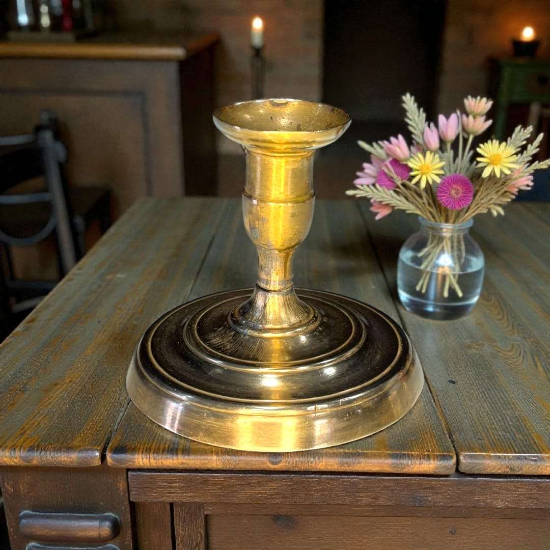 Palmatoria antigua de metal dorado con mango en relieve sobre mesa rústica frente a chimenea encendida, ideal para decoración clásica.