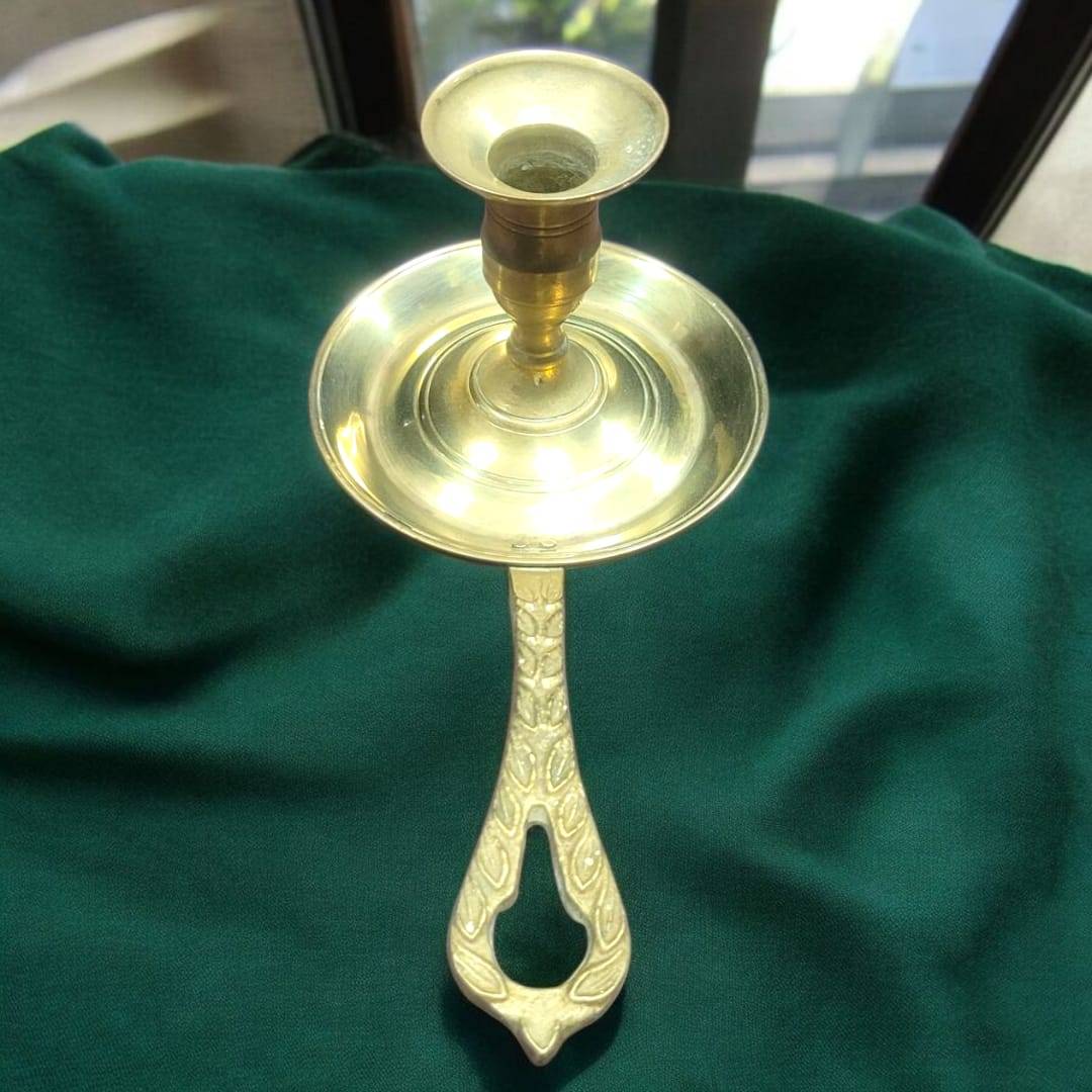 Palmatoria de metal dorado con mango calado grabado vintage sobre mantel verde. Diseño clásico ideal para decoración de interiores elegantes.