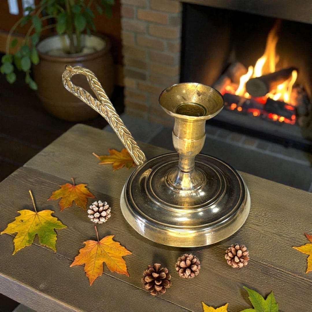 Palmatoria de metal dorado con mango decorado en relieve, rodeada de hojas otoñales y piñas, ideal para decoración de temporada.