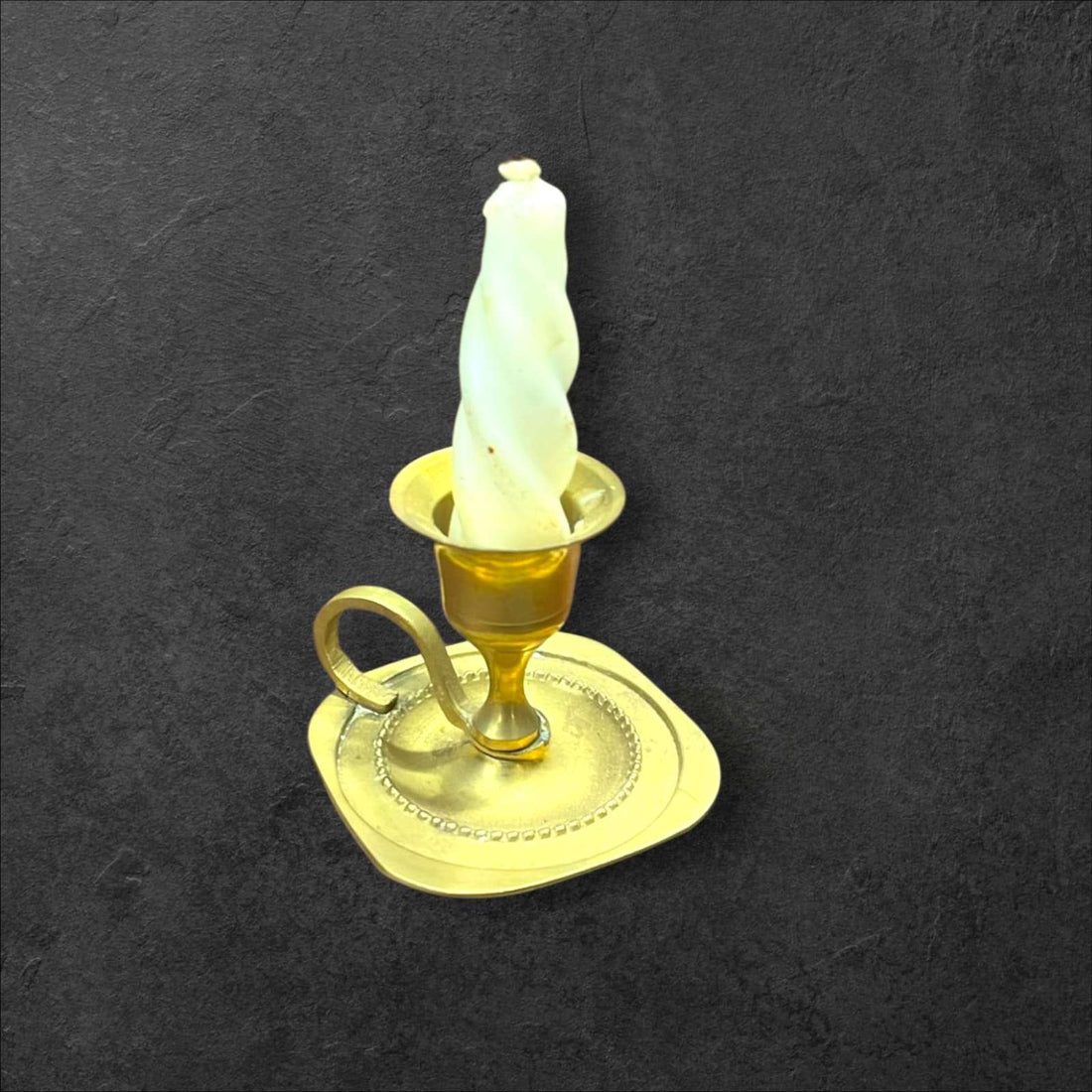 Palmatoria de metal dorado pequeña, vintage y decorativa con vela blanca en espiral sobre fondo oscuro. Ideal para decoración clásica del hogar.