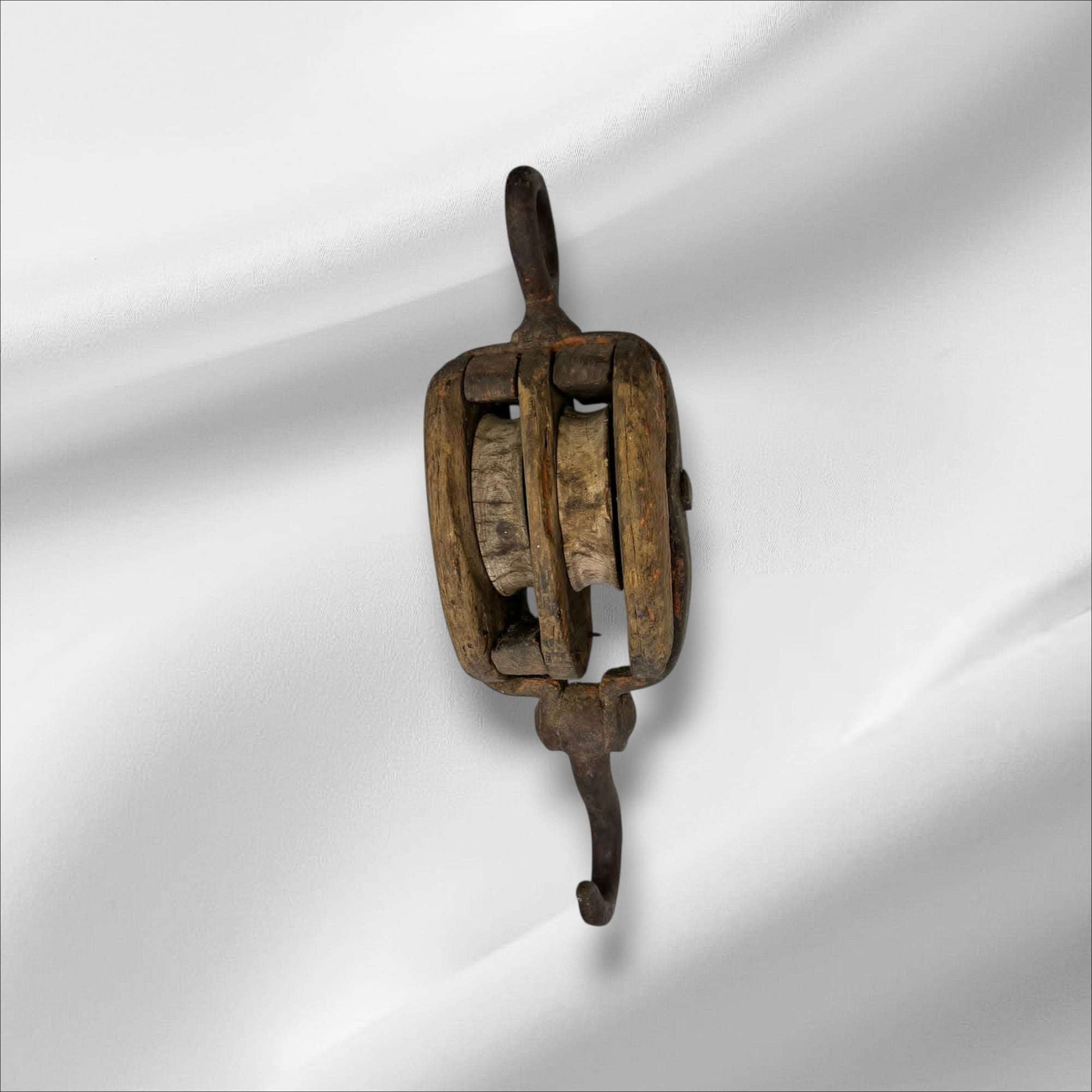 La polea doble antigua de madera y hierro es una pieza auténtica de ingeniería tradicional, utilizada en barcos y talleres para elevar cargas pesadas con mínima fuerza. Este aparejo de poleas combina la robustez del hierro forjado con la nobleza de la madera envejecida, mostrando el arte del trabajo manual y la precisión funcional de otra época.

Su estructura, compuesta por dos roldanas de madera maciza encajadas en un cuerpo sólido, permite una distribución equilibrada del peso y una operación suave. Cada