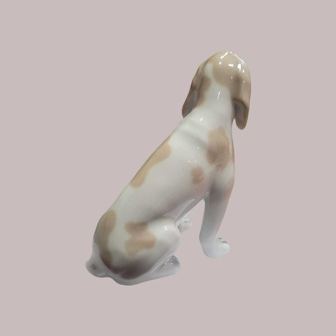 Perro de porcelana Lladró sentado en acabado brillante, figura decorativa con esmalte suave y detalles realistas en tonos beige y blanco.