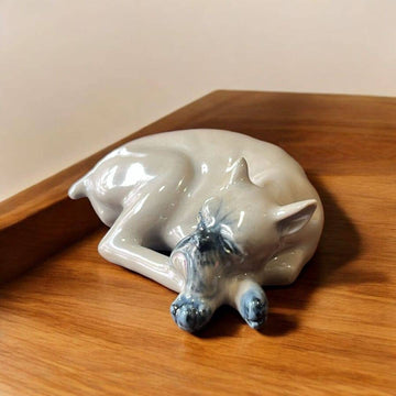 Escultura de porcelana Leonardo PEYRO de un Boxer dormido, con acabado vidriado brillante, sobre superficie de madera. Decoración elegante para hogar.