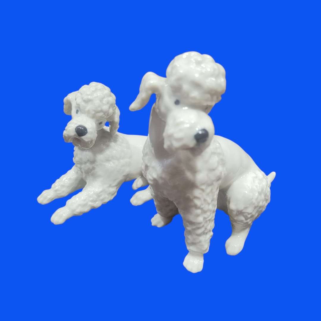 Pareja de perros caniche Marilyn de porcelana blanca en posición sentada y acostada, ideal para decoración elegante y coleccionismo.