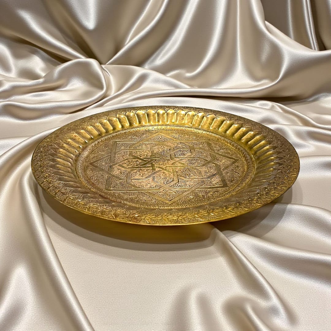 Plato árabe de metal dorado con grabados geométricos sobre fondo satinado.