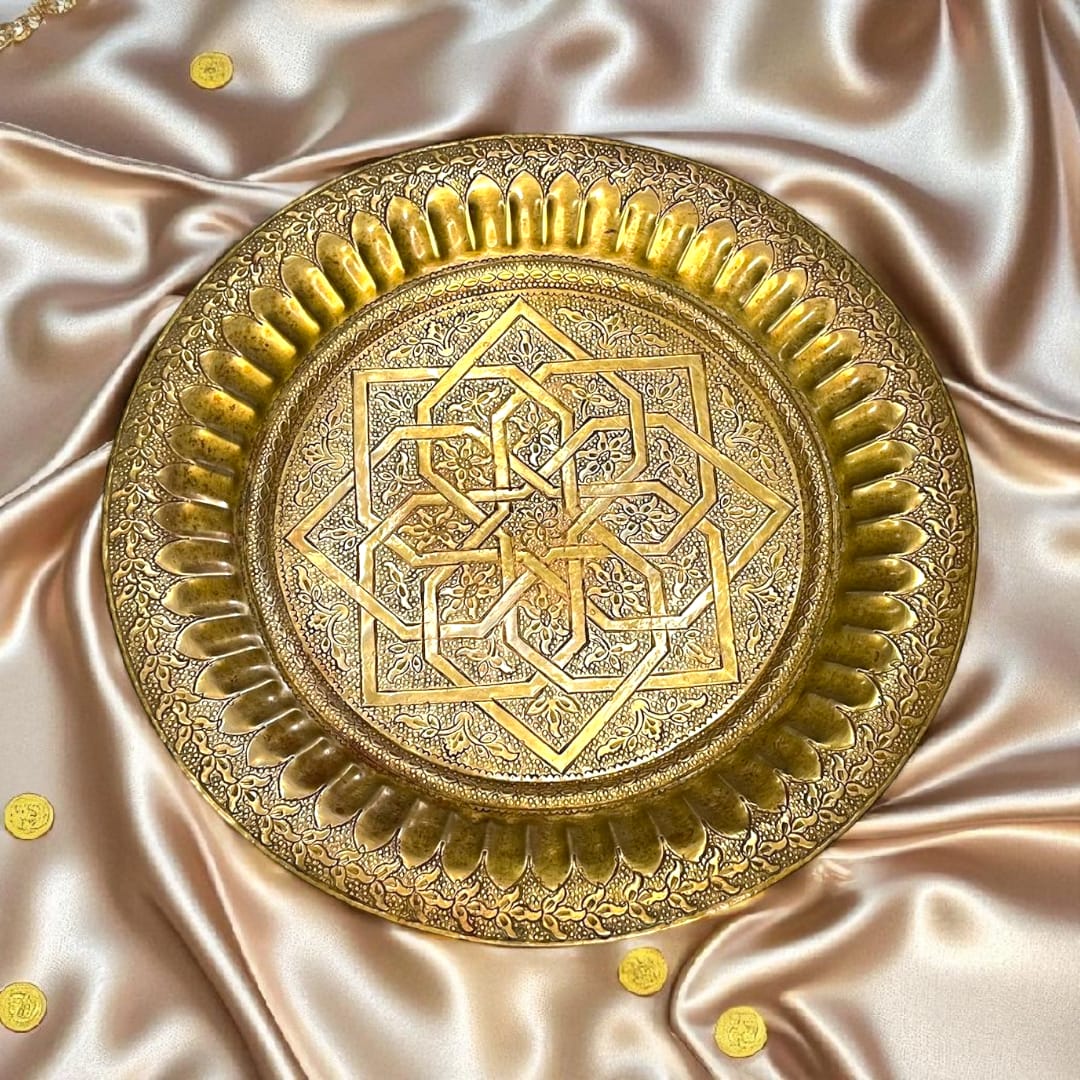 Plato árabe de metal dorado con grabados geométricos sobre fondo satinado.