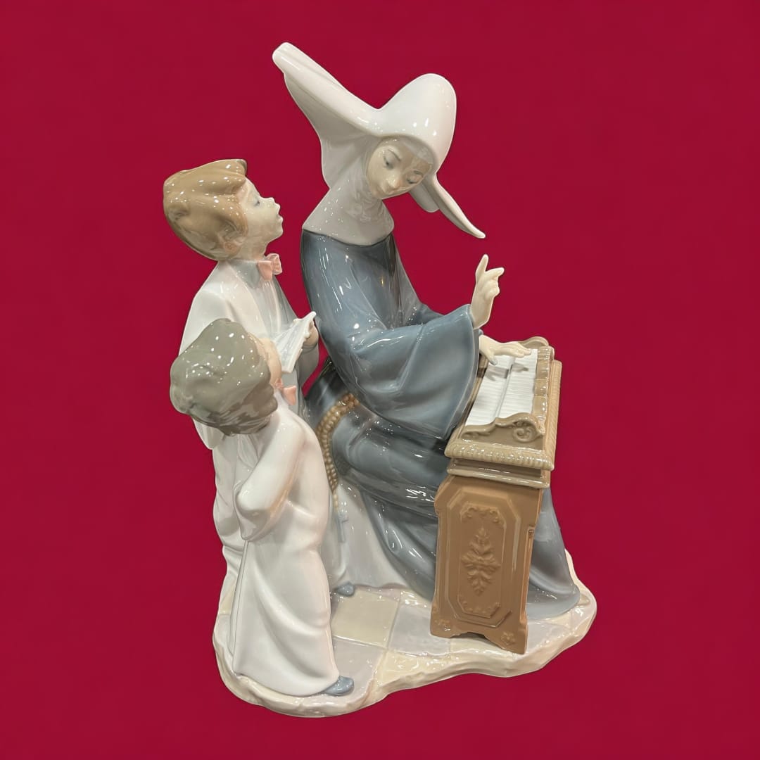 Escultura de porcelana Lladró con monja tocando el piano y dos niños atentos. Arte decorativo elegante y detallado para coleccionistas.