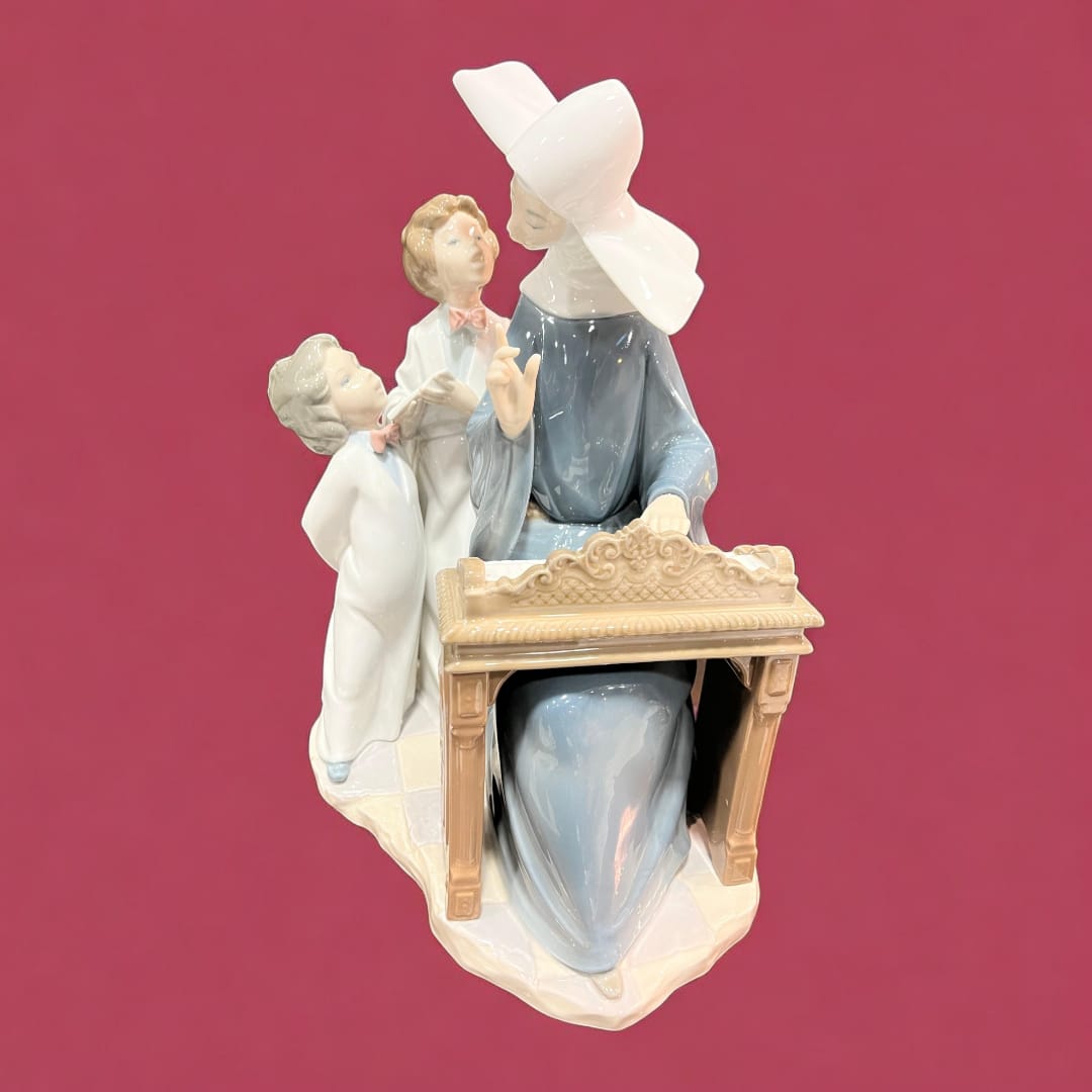 Escultura de porcelana Lladró con monja tocando el piano y dos niños atentos. Arte decorativo elegante y detallado para coleccionistas.