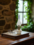 Quinqué de cristal antiguo decorando una mesa con gafas y libro.
