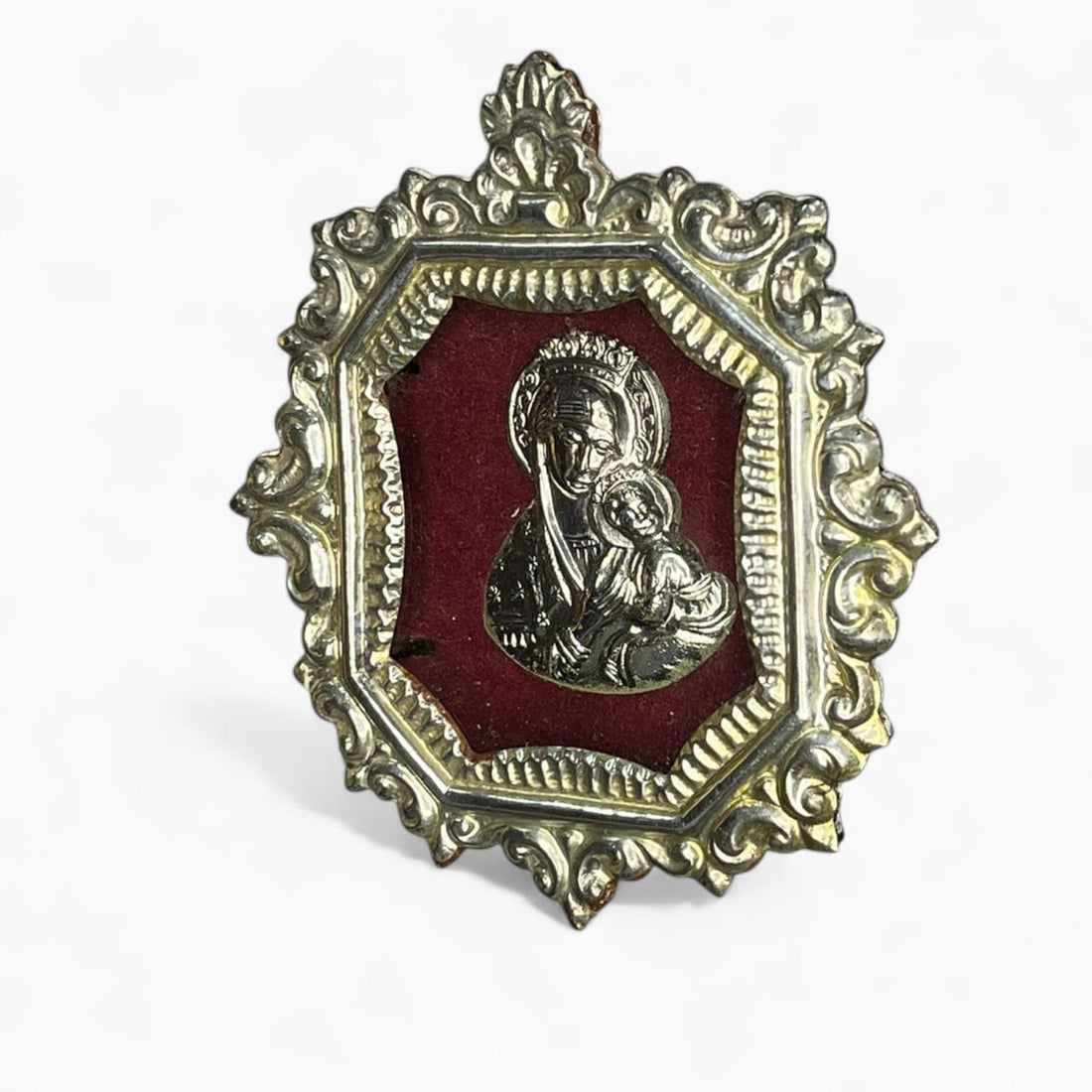 Relicario Virgen con Niño en marco de metal plateado y fondo burdeos.