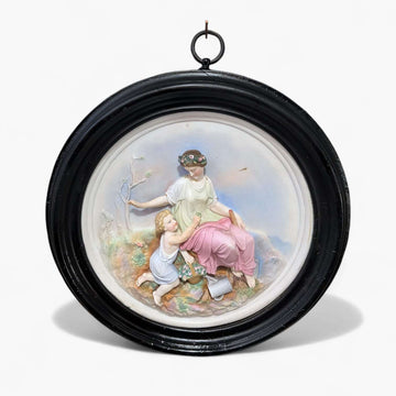 Relieve de porcelana restaurado con escena clásica único en marco oval negro, muestra figura femenina sentada con niño en paisaje natural.