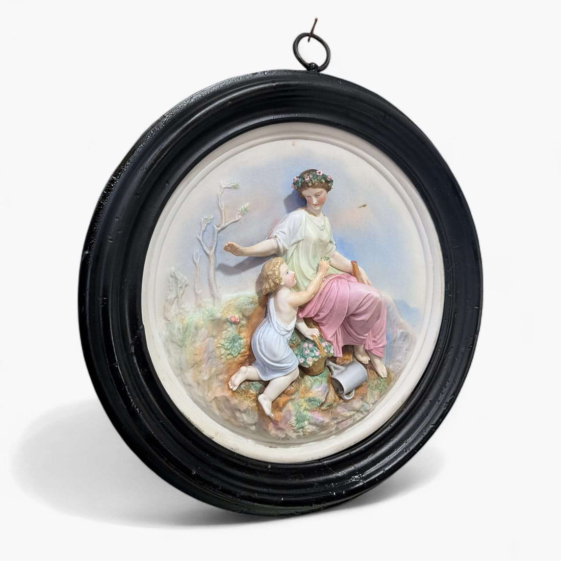 Relieve de porcelana restaurado con escena clásica único en marco oval negro, muestra figura femenina sentada con niño en paisaje natural.