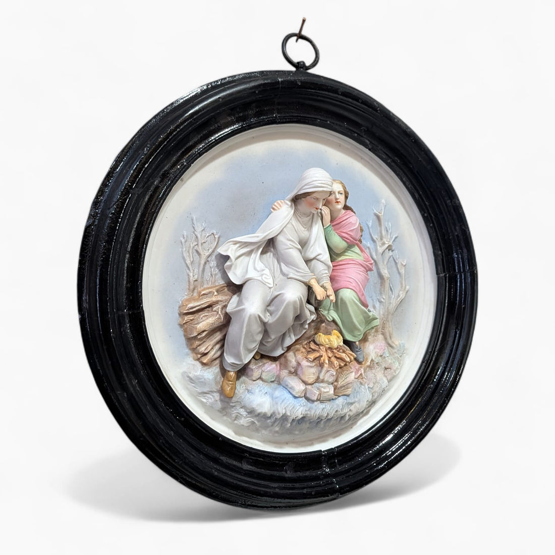 Relieve de porcelana antiguo restaurado con escena figurativa de dos figuras sentadas junto al fuego, en marco oval negro decorativo.