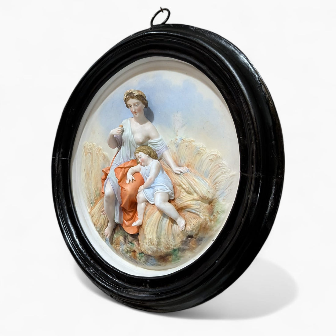 Relieve de porcelana antiguo restaurado escena materna con madre e hijo en campo de trigo, enmarcado en marco negro circular clásico. Decoración mural elegante para interiores vintage.