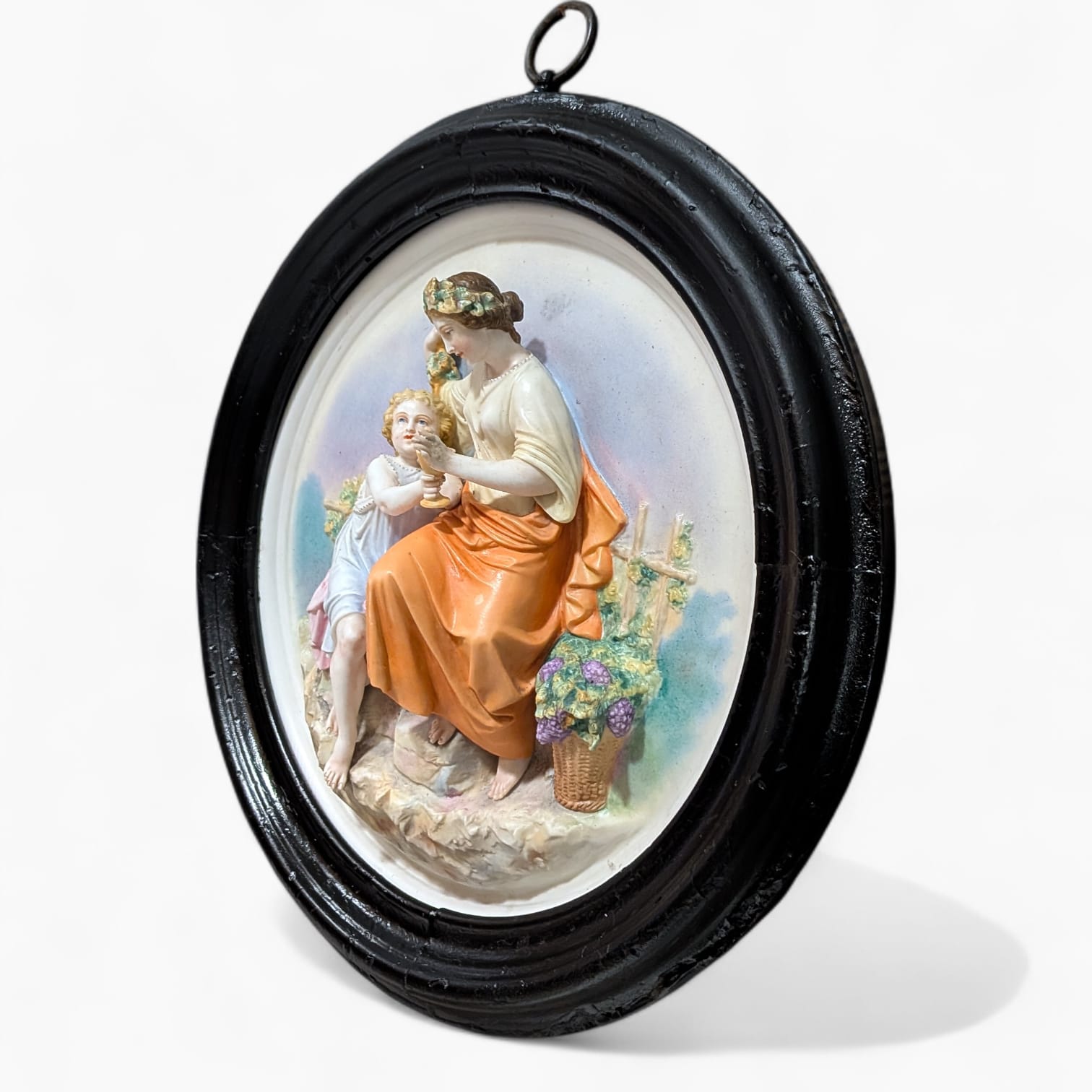 Relieve mural de porcelana restaurado con escena figurativa en alto relieve, marco circular negro y estilo decorativo clásico para interiores.