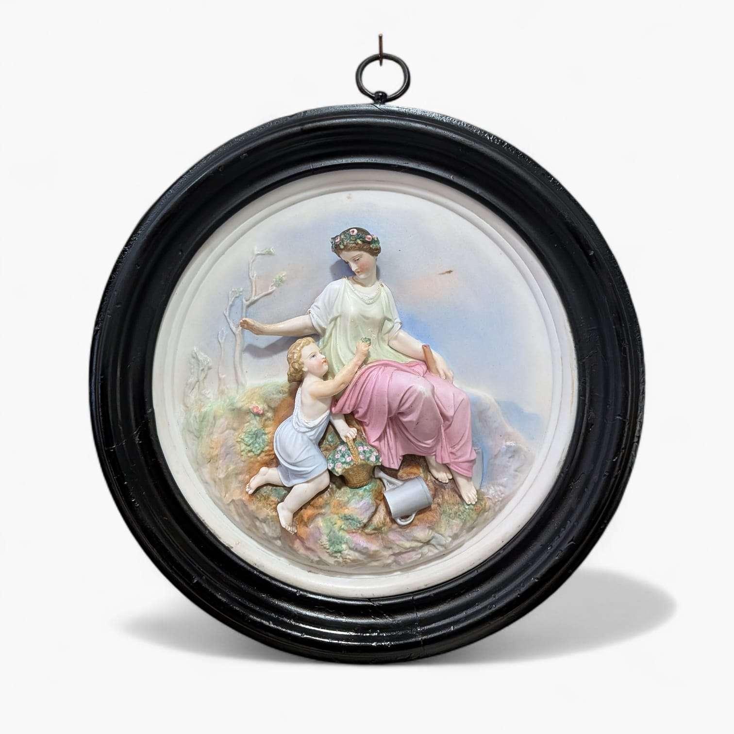 Relieve de porcelana restaurado con escena clásica único, mujer sentada y niño en entorno natural, marco negro listo para colgar en pared.
