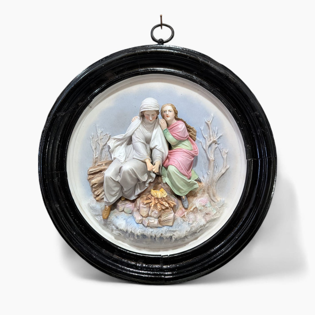 Relieve de porcelana antiguo restaurado con escena figurativa de dos figuras sentadas junto al fuego, en marco oval negro decorativo.