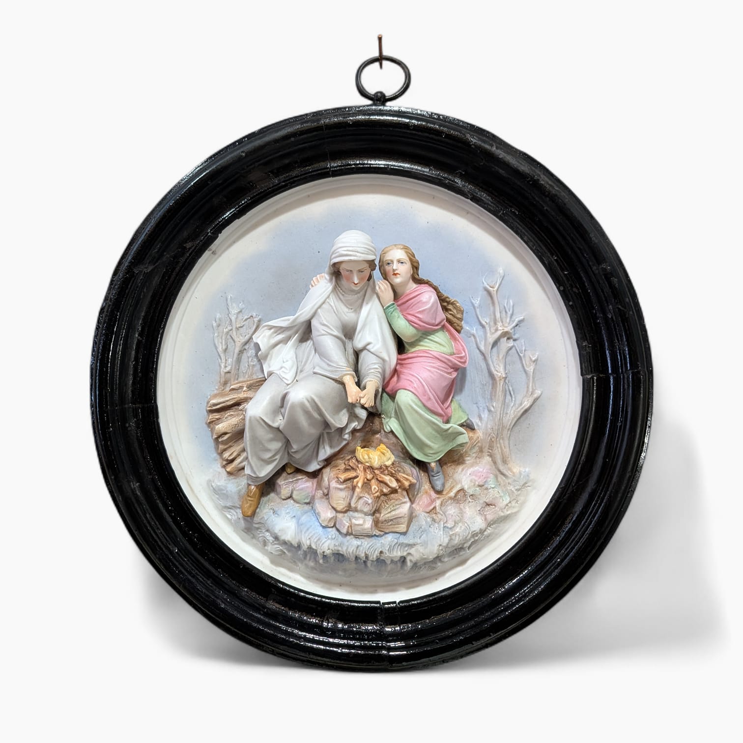 Relieve de porcelana antiguo restaurado con escena figurativa de dos figuras sentadas junto al fuego, en marco oval negro decorativo.