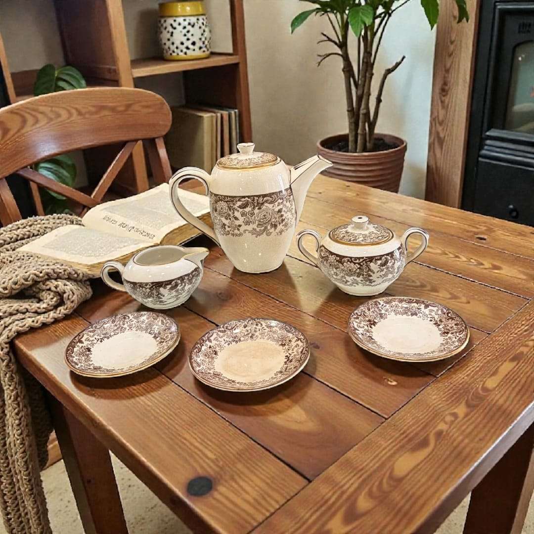 Juego de café Cartuja de Sevilla Pickman con loza decorada floral sobre mesa rústica. Elegancia histórica para decoración de hogar y coleccionistas.