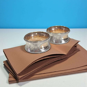 Servilleteros de metal plateado – pareja elegante sobre fondo azul.