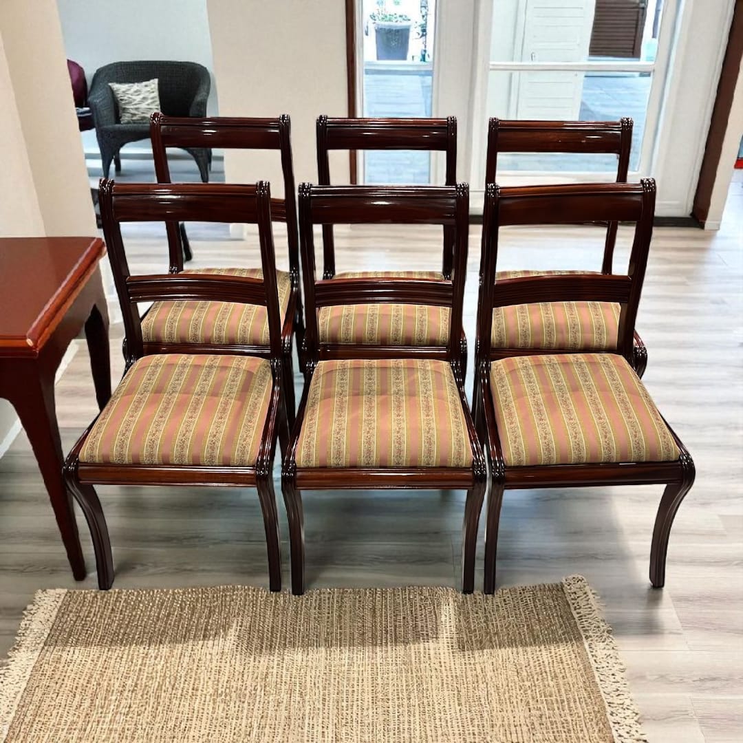 Lote de seis sillas de caoba tapizadas vistas de frente sobre alfombra clara.
