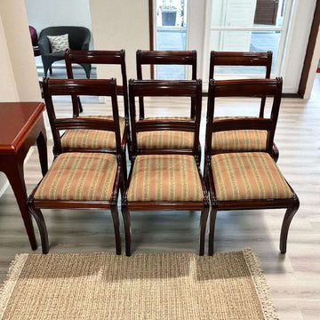 Lote de seis sillas de caoba tapizadas vistas de frente sobre alfombra clara.