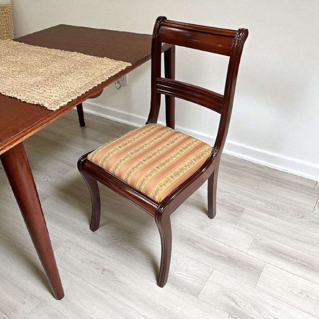 Silla de caoba tapizada junto a mesa de comedor clásica.