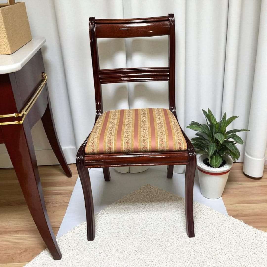 Vista individual de silla de caoba tapizada con fondo neutro y planta decorativa.