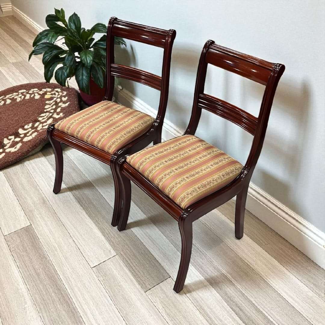 Dos sillas de caoba tapizadas ubicadas junto a pared y planta verde.