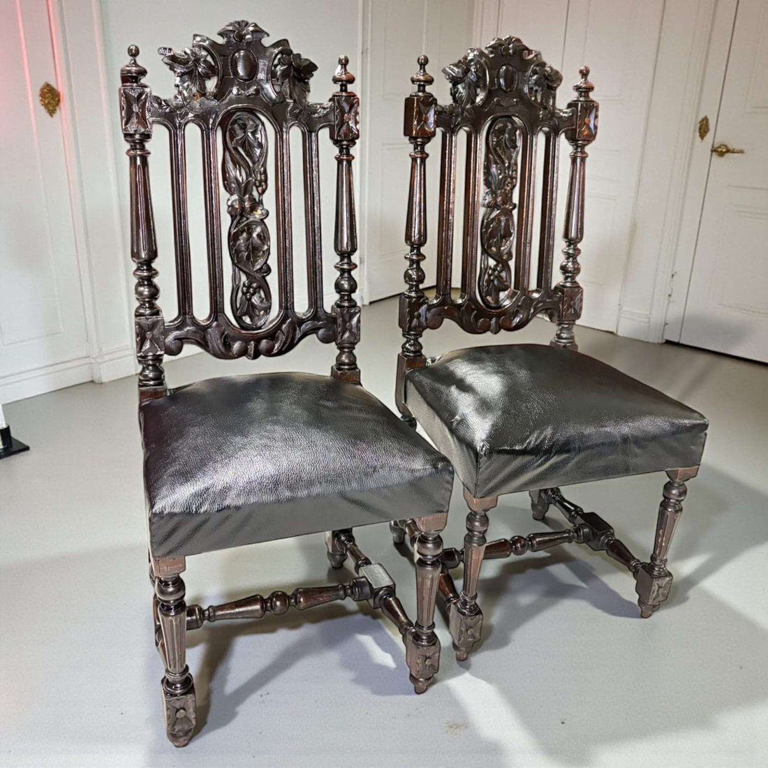 Pareja de Sillas Castellanas antiguas del siglo XIX talladas en madera oscura con respaldo ornamentado y asiento de cuero original. Decoración ideal para interiores clásicos.