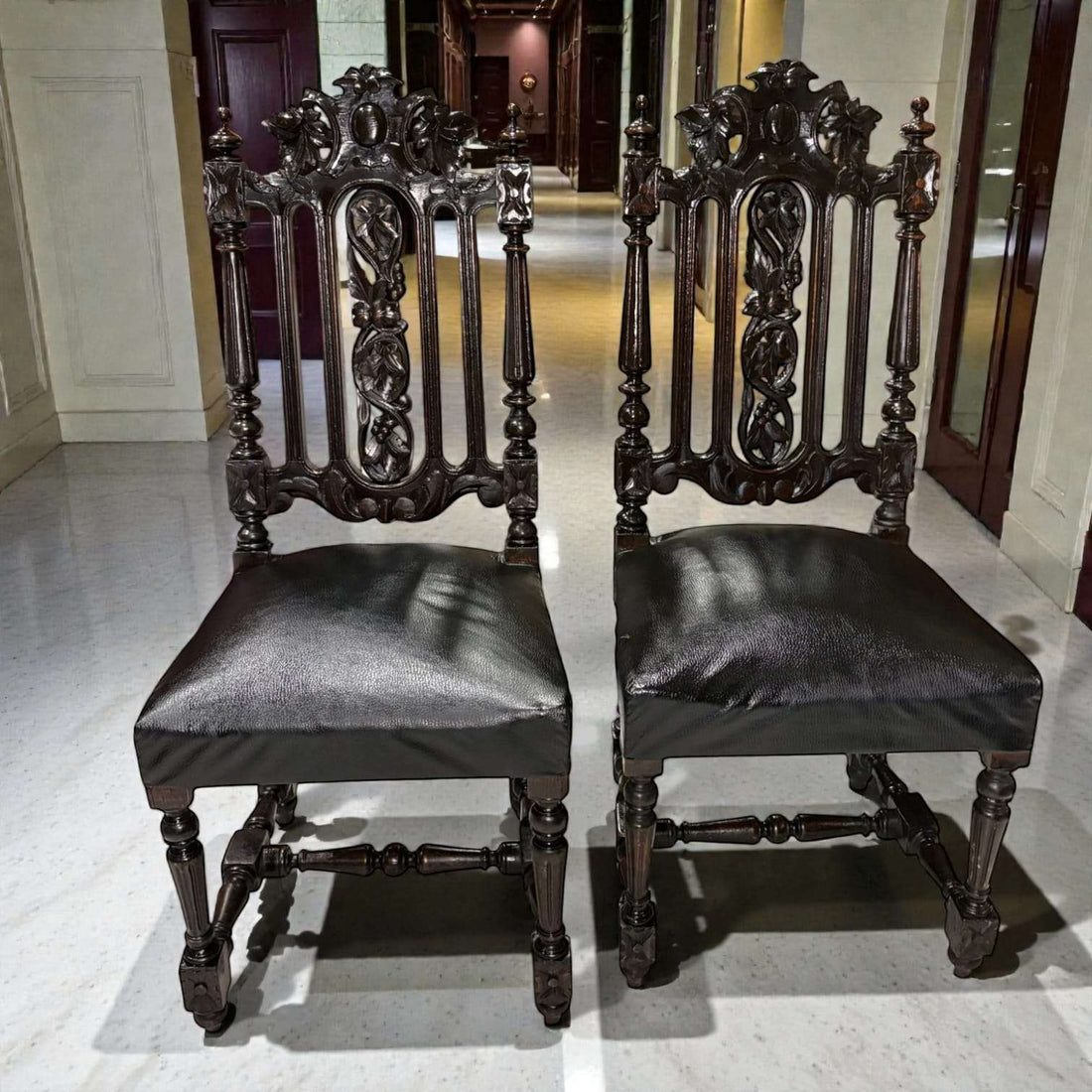 Pareja de Sillas Castellanas antiguas del siglo XIX talladas en madera oscura con respaldo ornamentado y asiento de cuero original. Decoración ideal para interiores clásicos.