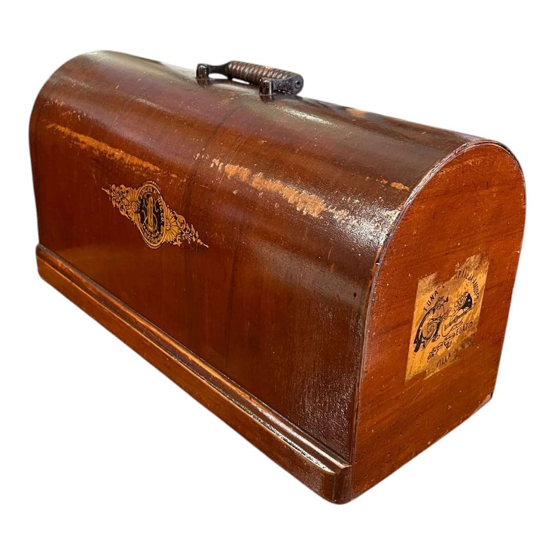 Vista en ángulo de la tapa de máquina de coser Singer con detalles dorados y etiqueta lateral, pieza original única para decoración clásica.