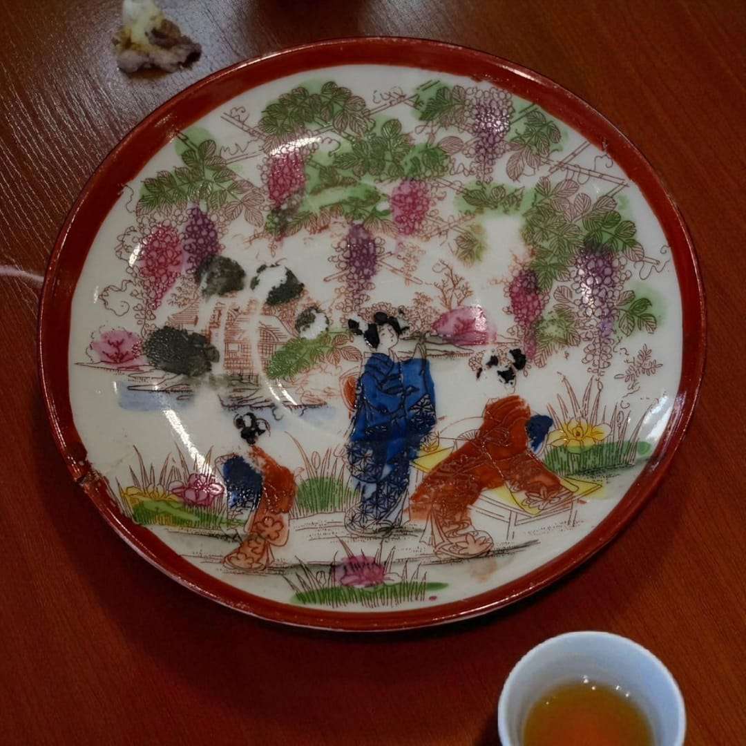 Plato decorativo de porcelana japonesa con diseño oriental pintado a mano, mostrando figuras tradicionales bajo glicinas. Ideal para decoración artística.