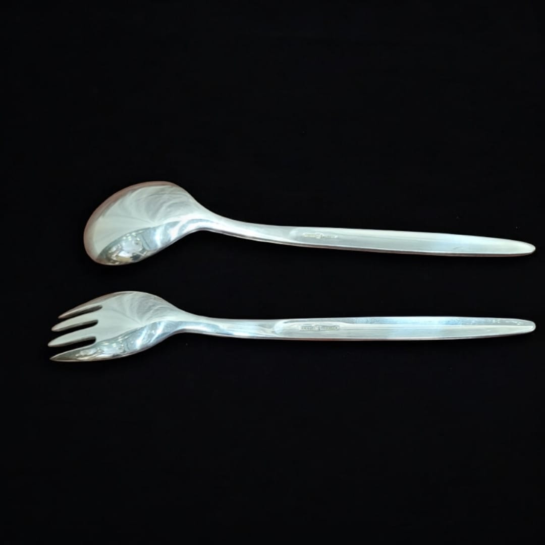 Juego de cuchara y tenedor para ensalada en metal plateado con diseño elegante sobre fondo negro. Ideal para servir ensaladas con estilo.