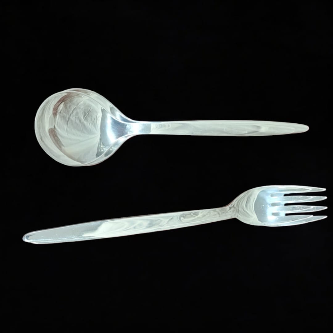 Juego de cuchara y tenedor para ensalada en metal plateado con diseño elegante sobre fondo negro. Ideal para servir ensaladas con estilo.