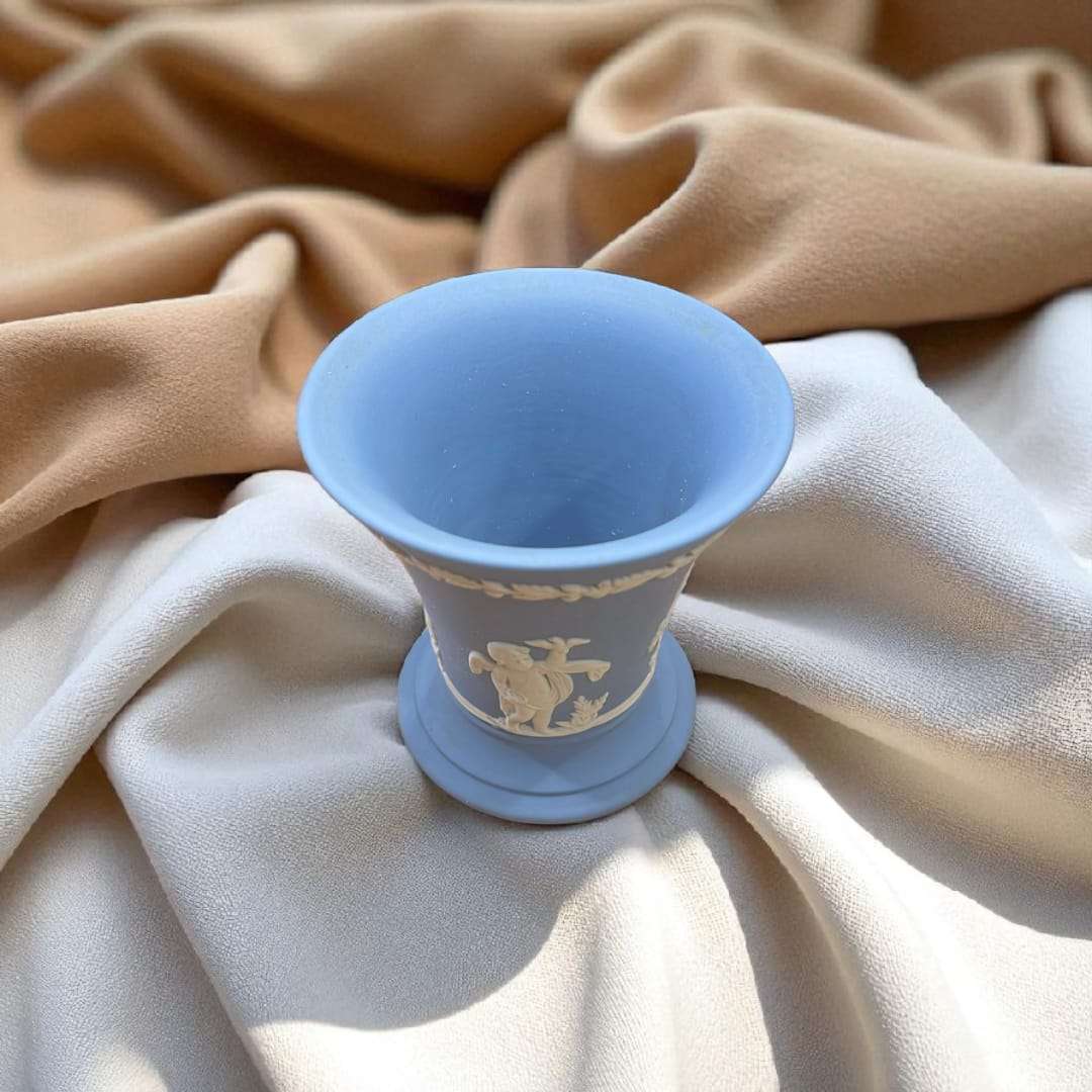 Jarrón Wedgwood azul jaspeado con relieve estilo clásico único iluminado por luz natural, sobre tela en tonos neutros para decoración refinada.